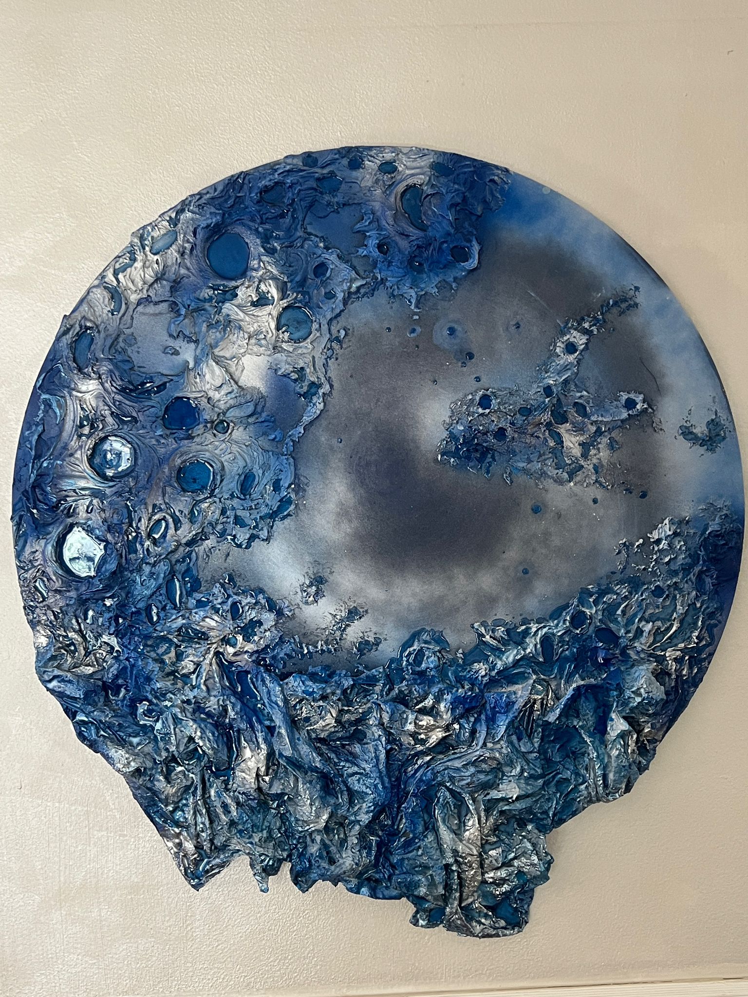 Circular blue and silver textured sculpture with crater-like indentations and crumpled foil edges?